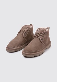 Braune Wildleder-Stiefeletten mit Kunstfellfutter, runden Schnürsenkeln, Metallösen und einer strukturierten Gummisohle für besseren Halt.