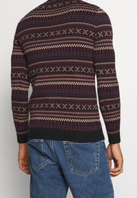 Pull en laine tricoté en bordeaux, crème et noir avec des motifs géométriques. Présente des poignets et un ourlet côtelés. Vue de dos montrant la texture détaillée du tricot.