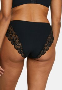 Bas de bikini noir côtelé avec une bordure en dentelle festonnée. La dentelle présente un motif floral détaillé le long des bords.