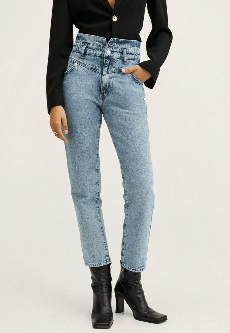 Hochtaillierte blaue Jeans aus Denim mit leichter Textur, mit Knopfverschluss, Fronttaschen und schmal zulaufendem Bein. Getragen mit schwarzen Absatzstiefeln.