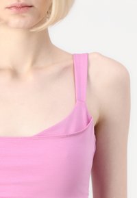 Rožinė tankinė palaidinė su plonomis petnešėlėmis, pagaminta iš sklandžios medvilnės audinio. Turi kreivą iškirptę ir be siūlių pečių dizainą.