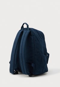 Mørkeblå fløjlsrygsæk med to polstrede skulderremme, et topgreb og sidelommer til opbevaring. Glat tekstur med en struktureret form.