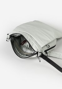 Helles grauer Rucksack mit weicher Textur, Reißverschlussöffnung und verstellbarem Träger. Das Innere enthält eine Reißverschlusstasche und einen elastischen Stauraum.