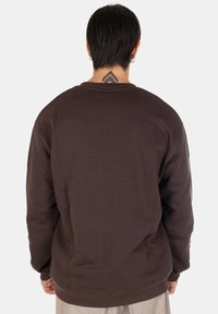 Felpa marrone a girocollo con vestibilità rilassata e polsini a costine, caratterizzata da una texture liscia e priva di motivi o dettagli visibili.
