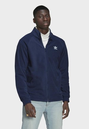 Navy blue fleece jacket with full zip, high collar, and white logo on the left chest. Features elastic cuffs and side pockets.