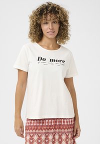 Tricou din bumbac crem, cu mâneci scurte și guler rotund; prezintă un text negru: „Fă mai mult din ceea ce te face fericit” cu accente decorative.
