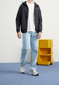 Czarna wodoodporna kurtka z kapturem, biała koszulka, jasnoniebieskie dżinsy oraz szare buty sportowe. W tle żółta szafka.