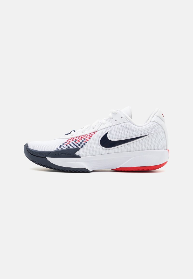 Baskets basses Nike blanches avec un swoosh noir, un motif rouge et bleu sur le côté, et des détails noirs et rouges sur la semelle, vues de profil.