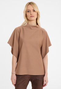 Brown, short-sleeved top with a high neckline and flowing design. Soft texture and smooth fabric. Paired with dark brown pants.