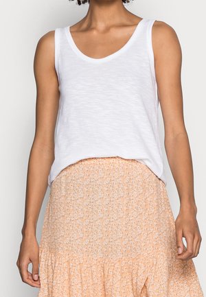 Vrouw draagt een mouwloos wit topje gecombineerd met een hooggesneden perzikkleurige rok met kleine witte bloemenprints.