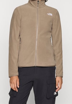 Chaqueta polar marrón con cremallera y bolsillos laterales, con el logo de The North Face en el pecho, combinada con pantalones cargo negros con bolsillos de solapa.
