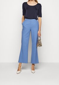 Haut à manches courtes navy, pantalon large bleu clair, et sac à main beige. Le modèle porte des talons aiguilles beiges. Tissu lisse avec une coupe ajustée.