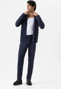 Chemise bleue marine à boutons assortie à un pantalon bleu marine. La chemise a des manches longues et une poche à l'avant. Le modèle porte un débardeur blanc en dessous.
