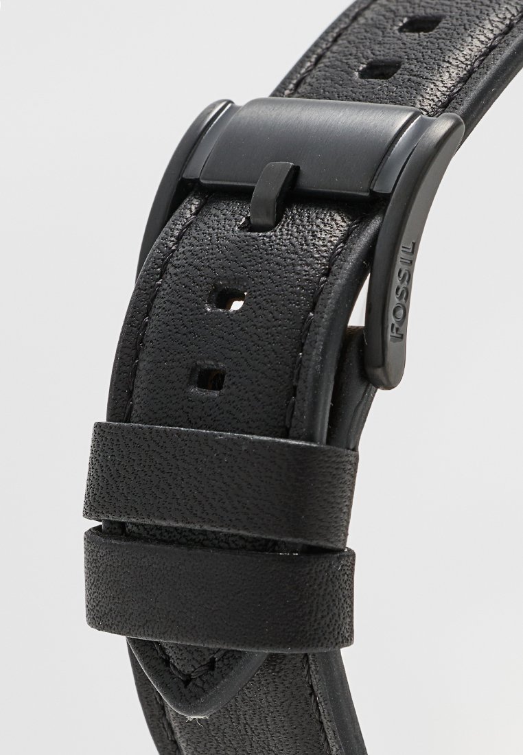 Correa de reloj de cuero negro con acabado texturizado, que presenta varios agujeros para ajuste y una hebilla negra mate con la marca "FOSSIL".