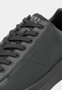 Basket en cuir noir avec lacets noirs, avec logo embossé "GUESS" et texte "EST. 1981" sur la languette.