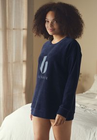 Felpa a maniche lunghe di colore blu navy con tessuto lavorato e logo sul petto. Presenta scollo rotondo e polsini aderenti. Vestibilità casual e comoda.