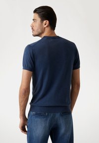 Suéter de manga corta azul marino con un tejido suave y texturizado, cuello redondo y dobladillo acanalado, combinado con jeans de mezclilla azul claro.