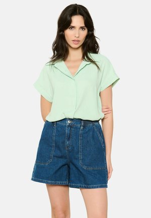 Mintsko zelena kratka majica s kratkimi rokavi in ovratnikom, kombinirana z visokim pasom denim kratkimi hlačami, ki vsebujejo dva sprednja žepa in ravno rez.