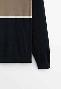 Pull à manches longues avec une partie inférieure noire, une partie supérieure beige et une fine bande blanche séparant les deux couleurs sur un fond blanc.