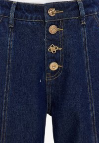 Pantalones de mezclilla de tiro alto en azul oscuro, con cuatro botones dorados ornamentados, detalles cosidos y un ajuste estructurado con bolsillos traseros.