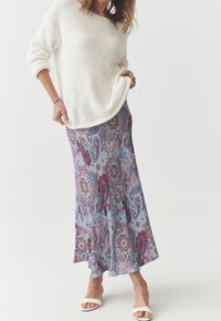 Un pull en tricot blanc surdimensionné, associé à une jupe maxi en imprimé cachemire bleu avec des accents roses et verts. Des sandales blanches simples.