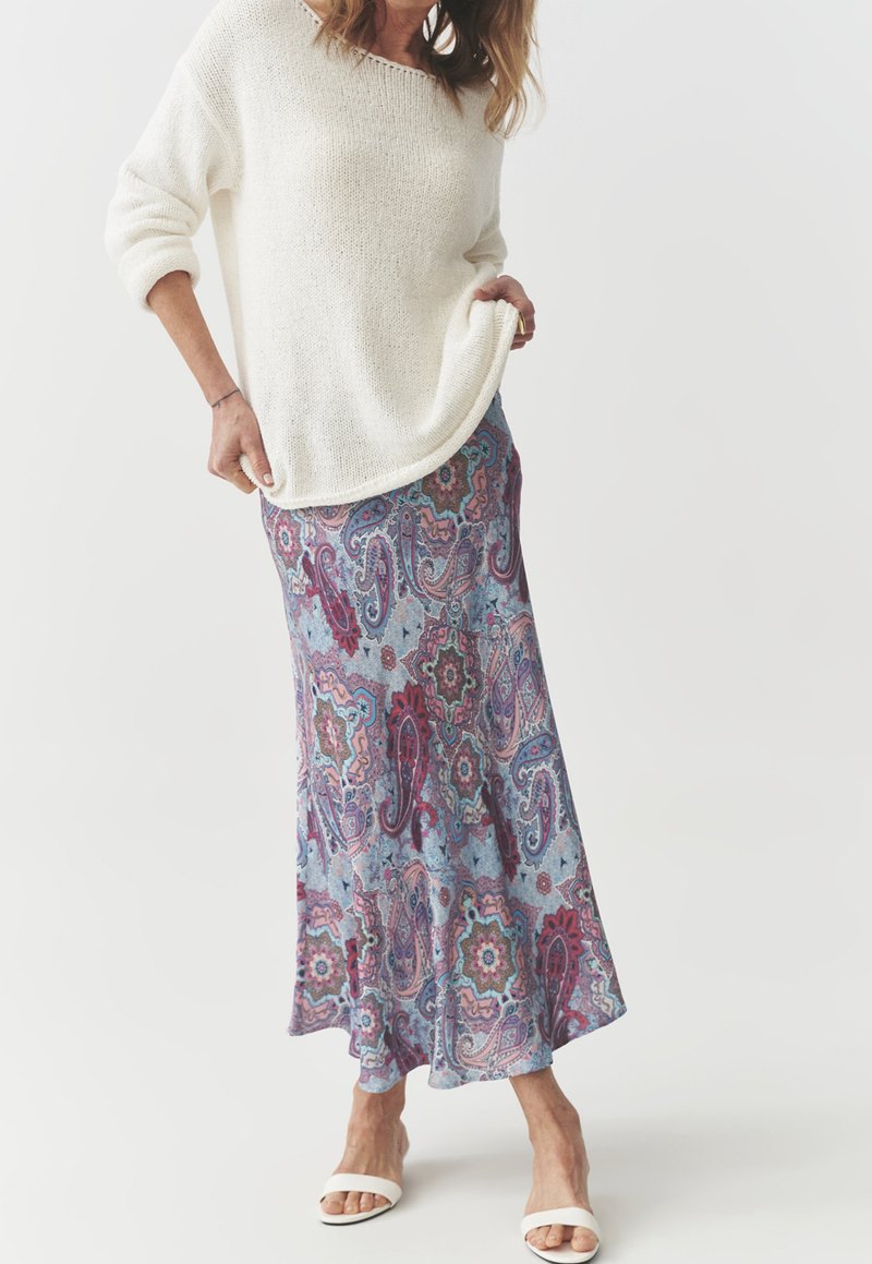 Un pull en tricot blanc surdimensionné, associé à une jupe maxi en imprimé cachemire bleu avec des accents roses et verts. Des sandales blanches simples.