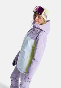 Kurtka narciarska w kolorze lawendowym i jasnoniebieskim, z zamkiem błyskawicznym, kapturem i logo Roxy. Stylizowana z dopasowanymi rękawicami i goglami narciarskimi.