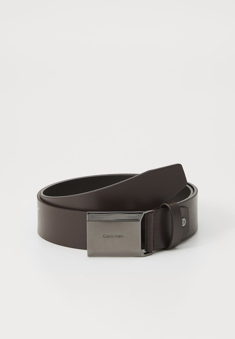 Barna bőr öv, sima, téglalap alakú ezüst csattal, melyen dombornyomott logó található. Az öv szíja textúrált felülettel és klasszikus dizájnnal rendelkezik.