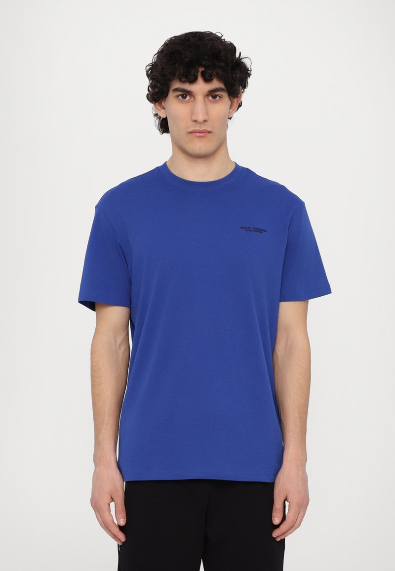 Μπλε βαμβακερό μπλουζάκι με κοντά μανίκια, στρογγυλή λαιμόκοψη και διακριτικό μαύρο λογότυπο στη δεξιά πλευρά του στήθους, σχεδιασμένο για άνετη εφαρμογή.