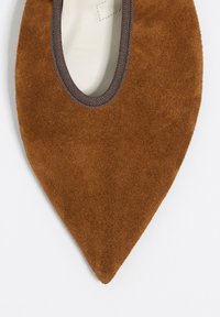 Zapato plano de ante marrón con punta en pico, abertura redondeada y ribete oscuro contrastante alrededor del borde superior, con un forro interior liso.
