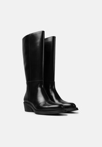 Černé kožené kozačky po kolena s hladkým povrchem, zaoblenou špičkou a nízkým vrstveným podpatkem. Mají vertikální švy po stranách.