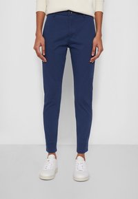 Granatowe spodnie bawełniane o dopasowanym kroju, z zapięciem na guziki i kieszeniami wkładanymi, zestawione z białymi trampkami.