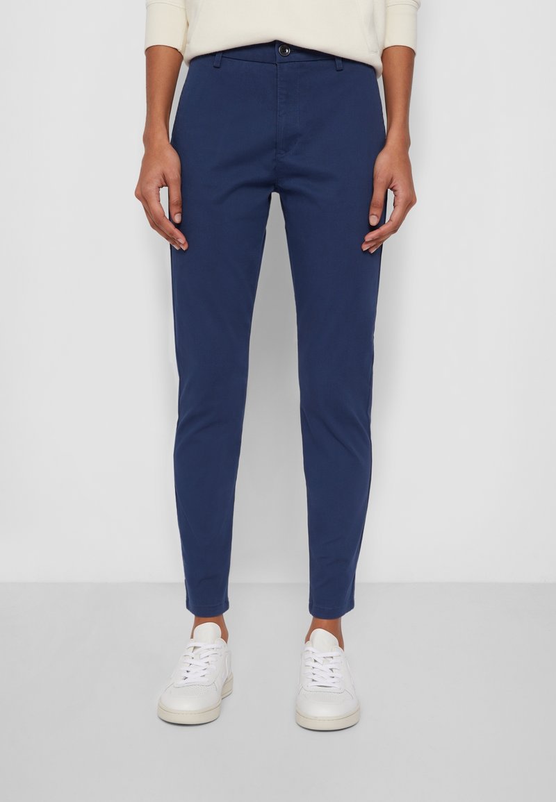 Granatowe spodnie bawełniane o dopasowanym kroju, z zapięciem na guziki i kieszeniami wkładanymi, zestawione z białymi trampkami.