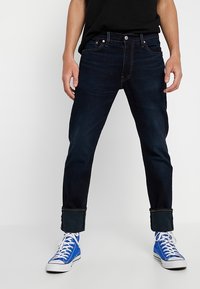Mörkblå denimjeans med rak passform, uppvikt nederkant och kontrasterande sömmar. I kombination med vita och blå sneakers.