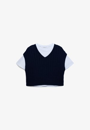 Maglione corto senza maniche in maglia blu navy con scollo a V indossato sopra una T-shirt bianca a maniche corte, caratterizzato da un motivo a trecce e orlo a costine.