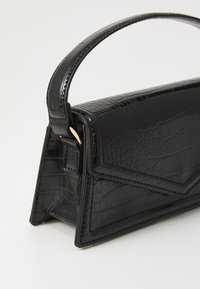 Black handbag made of faux leather with a crocodile texture, featuring a structured shape, top handle, and angled side panels.