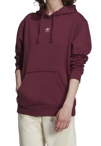 Mörkröd huvtröja i bomullsmaterial med känguruficka, snoddhuva och en liten guld Adidas-logotyp på bröstet. Mjukt material.