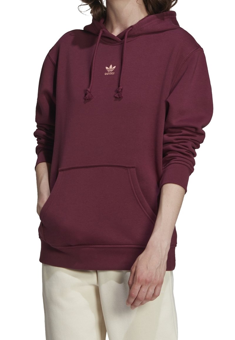 Mörkröd huvtröja i bomullsmaterial med känguruficka, snoddhuva och en liten guld Adidas-logotyp på bröstet. Mjukt material.