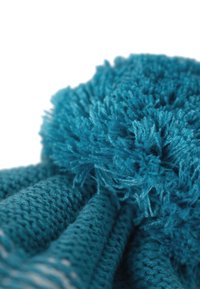 Teal knitted scarf featuring textured yarn and a pom-pom detail. The material is soft and fluffy, with a ribbed pattern along the edges.