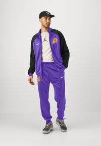 Purpurový Nike teplákový komplet s čiernymi akcentmi, s grafikou basketbalu a logom Jordana. Šedé tenisky dotvárajú športový vzhľad.