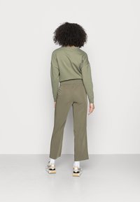 Sweatshirt verde-oliva com ombros caídos, combinado com umas calças cropped a condizer. Modelo a usar meias brancas e sapatilhas com detalhes pretos.