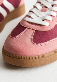 Sneaker rosa e bordeaux con texture in suede, lacci bianchi e suola in gomma con dettagli scanalati. Accentuato da occhielli ovali.