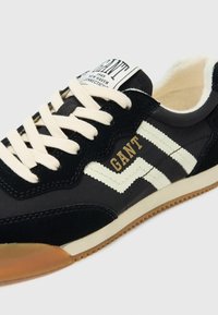 Black sneaker with white and beige accents, suede and textile material, laces, and a gum rubber sole. Features "GANT" branding on tongue.