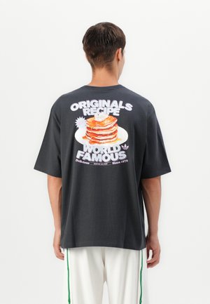 Fekete oversized póló, amelynek hátsó részén színes palacsinta grafika található a "ORIGINALS RECIPE WORLD FAMOUS" felirattal. Rövid ujjú.