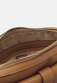 Interior de bolso de cuero marrón, con un bolsillo con cremallera y forro de satén color marrón claro con un sutil patrón repetitivo de logotipos. Detalle de cremallera dorada.