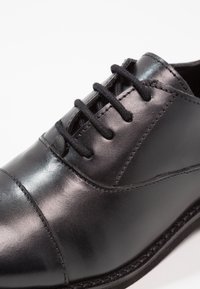 Black polished leather dress shoe with rounded cap toe and black laces against a white background.