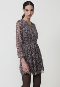 Vestido con estampado floral en gasa ligera, con escote en V, mangas largas transparentes y cintura ajustada, con una falda acampanada y un sutil brillo.