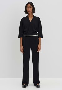 Zwarte v-hals top met brede mouwen, gecombineerd met hoge zwarte broeken. Glad materiaal, getailleerde fit en zwarte platte schoenen.