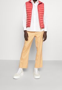 Red puffer vest over a white shirt, paired with light yellow plaid trousers and chunky white sneakers with grey accents.