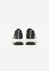 Baskets de sport noires avec une tige texturée, des bandes blanches en accent et une semelle rembourrée. La vue de l'arrière met en évidence la forme et les détails du design.